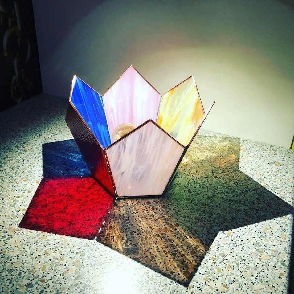 Geometric stained glass candle holder projecting colorful light patterns on a speckled surface.