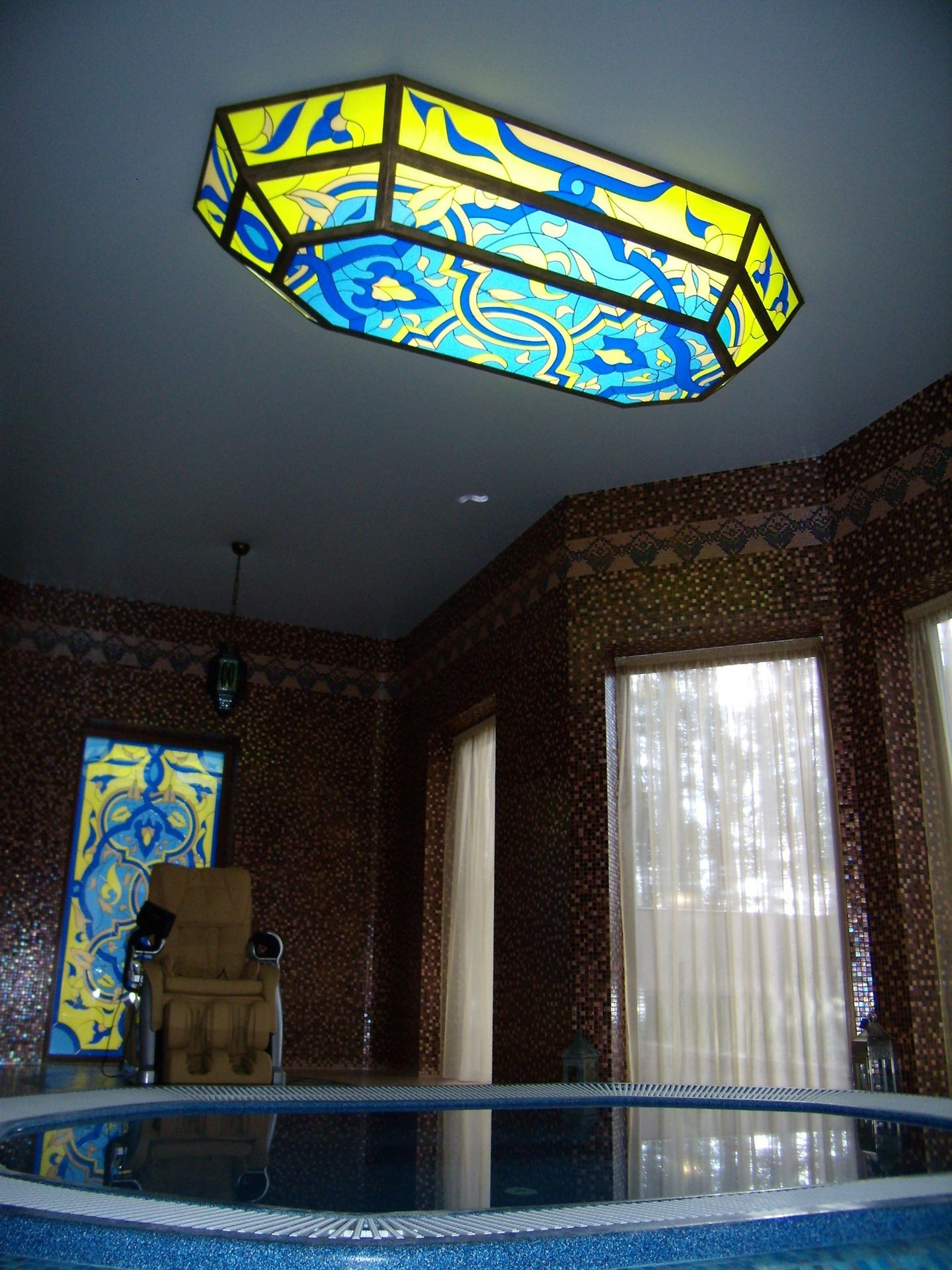 Room with mosaic walls, a jacuzzi, and a colorful stained glass ceiling light.